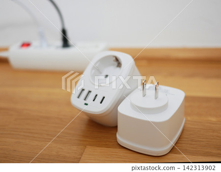 Universal travel adapter close up against the backdrop of a socket. Electric plug adapter, international plug socket gadget for travel. Universal travel adapter close up against the backdrop of a socket. Electric plug adapter, international plug socket gadget for travel. 142313902