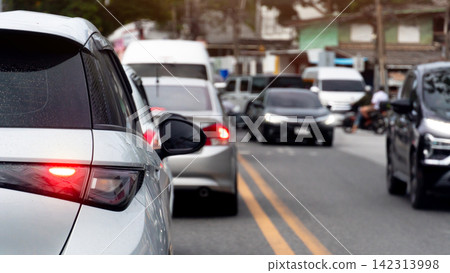 Rear view of hactback car with turn on brake light and stop on asphalt road. Vehicles are caught in a heavy traffic jam on an urban highway road during a bright daytime commute. 142313998