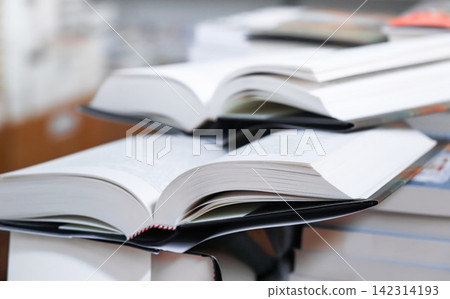 stack of books, close up. Open book on the table in library. Back to school concept. Open book on table with blur bookshelf background stack of books, close up. Open book on the table in library. Back to school concept. Open book on table with blur bookshelf background 142314193