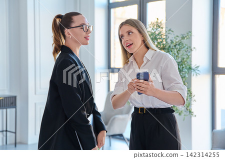 Two businesswomen looking at smartphone in modern office Two businesswomen looking at smartphone in modern office 142314255