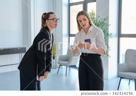 Two businesswomen looking at smartphone in modern office Two businesswomen looking at smartphone in modern office 142314256