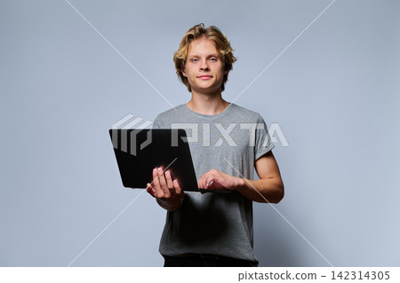 Portrait of teenage student holding open laptop and typing 142314305