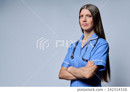 Three-quarter portrait of confident female nurse standing with folded arms on grey background Three-quarter portrait of confident female nurse standing with folded arms on grey background 142314338