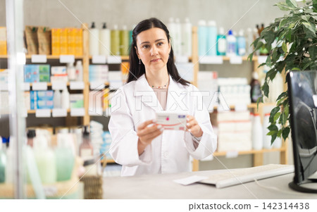 Middle-aged female pharmacist offering preparation in box Middle-aged female pharmacist offering preparation in box 142314438