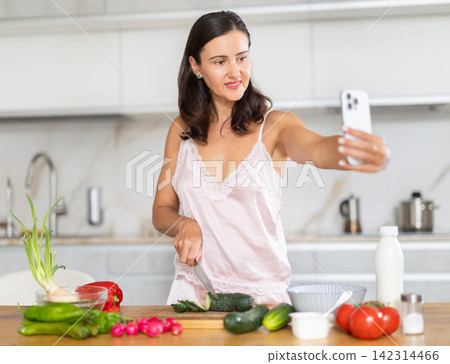 woman filming the process of making a salad in the kitchen on her mobile woman filming the process of making a salad in the kitchen on her mobile 142314466