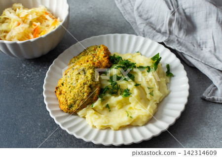 This plate features mashed potatoes, two turkey meatballs, and a side of fermented cabbage. Fresh herbs are sprinkled on top, creating a balanced meal choice This plate features mashed potatoes, two turkey meatballs, and a side of fermented cabbage. Fresh herbs are sprinkled on top, creating a balanced meal choice 142314609