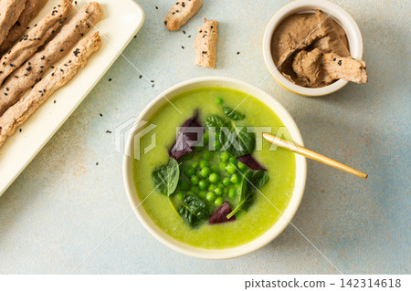 A bowl of creamy broccoli and green pea soup sits on a green plate. Next to it is liver pate in a small dish and grissini on a white platter. This meal provides healthy options A bowl of creamy broccoli and green pea soup sits on a green plate. Next to it is liver pate in a small dish and grissini on a white platter. This meal provides healthy options 142314618