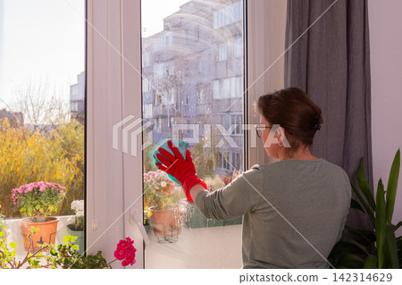 A person is cleaning the windows of an apartment balcony in the fall season. Flowers are present in pots, and the sun is shining on the scene A person is cleaning the windows of an apartment balcony in the fall season. Flowers are present in pots, and the sun is shining on the scene 142314629