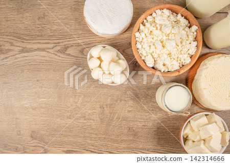 Assorted dairy products including cheese, cottage cheese, and milk displayed on a wooden table, showcasing various textures and forms in a natural setting Assorted dairy products including cheese, cottage cheese, and milk displayed on a wooden table, showcasing various textures and forms in a natural setting 142314666