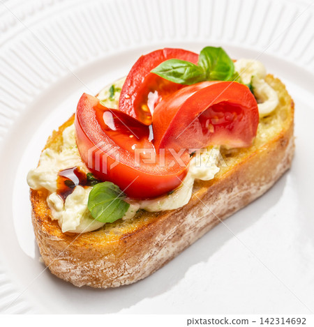 Fresh bruschetta topped with sliced tomatoes and basil on toasted bread served on a white plate with a textured rim, showcasing vibrant colors and appetizing presentation Fresh bruschetta topped with sliced tomatoes and basil on toasted bread served on a white plate with a textured rim, showcasing vibrant colors and appetizing presentation 142314692
