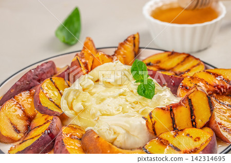 Grilled peaches served with creamy cheese and honey on a white plate, garnished with fresh mint leaves and honey in a small bowl Grilled peaches served with creamy cheese and honey on a white plate, garnished with fresh mint leaves and honey in a small bowl 142314695