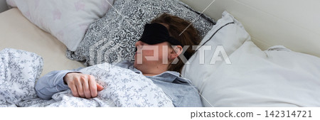 A middle-aged woman is sleeping soundly in her bed, wearing a sleep mask. She is surrounded by soft pillows and a warm blanket, taking a break from her daily routine, banner A middle-aged woman is sleeping soundly in her bed, wearing a sleep mask. She is surrounded by soft pillows and a warm blanket, taking a break from her daily routine, banner 142314721