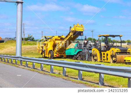 Large machines are operating on grass beside road during daytime with clear weather. Large machines are operating on grass beside road during daytime with clear weather. 142315295
