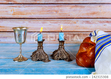 Ritual items are set on blue table two Shabbat candles, are lit beside cup, challah bread. Ritual items are set on blue table two Shabbat candles, are lit beside cup, challah bread. 142315308
