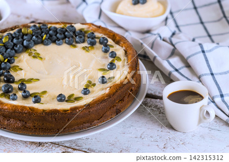 Enjoying cheesecake topped with blueberries, plate of coffee on table in kitchen. Enjoying cheesecake topped with blueberries, plate of coffee on table in kitchen. 142315312