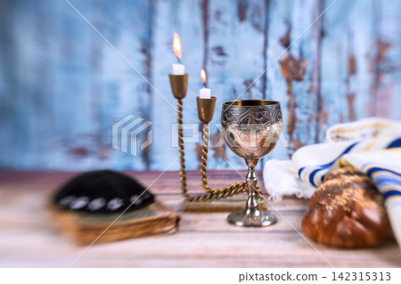 Silver cup with ritual candles next to challah bread, cloth on Shabbat table setting for meal at Jewish home. Silver cup with ritual candles next to challah bread, cloth on Shabbat table setting for meal at Jewish home. 142315313
