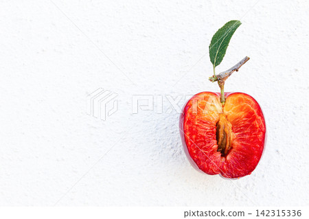 Ripe plum sliced open, showcasing its red interior, green leaf attached to stem Ripe plum sliced open, showcasing its red interior, green leaf attached to stem 142315336