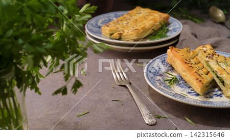 Flaky puff pastry stuffed with savory green filling on vintage patterned plates Flaky puff pastry stuffed with savory green filling on vintage patterned plates 142315646