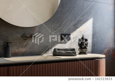 Bathroom vanity styled with folded towels and a Ganesha statue under soft light Bathroom vanity styled with folded towels and a Ganesha statue under soft light 142315653