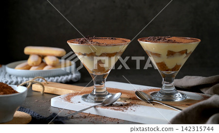Two stemmed cocktail glasses filled with tiramisu dessert on a white marble board Two stemmed cocktail glasses filled with tiramisu dessert on a white marble board 142315744