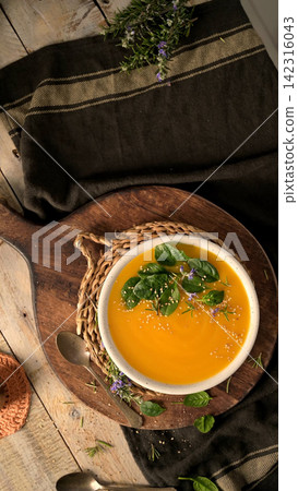 Creamy pumpkin soup served in a white bowl with spinach leaves and sesame seeds 142316043