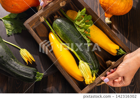 Woman holding wooden crate with fresh zucchini and squash Woman holding wooden crate with fresh zucchini and squash 142316302