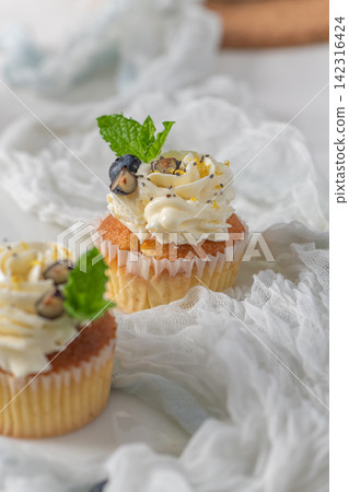 Cupcakes with white frosting and blueberries on white fabric background Cupcakes with white frosting and blueberries on white fabric background 142316424