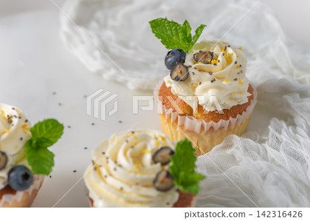 Fresh lemon cupcakes with white cream frosting, blueberries, and mint leaves Fresh lemon cupcakes with white cream frosting, blueberries, and mint leaves 142316426