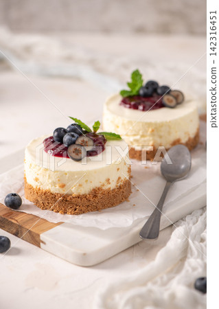 Mini cheesecakes with blueberry topping and mint leaves on a white board Mini cheesecakes with blueberry topping and mint leaves on a white board 142316451