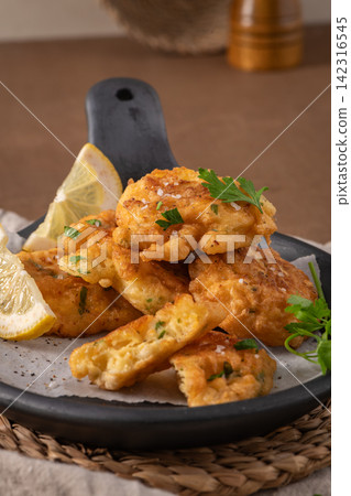 Golden crispy corn fritters served in a rustic black skillet with lemon wedges 142316545