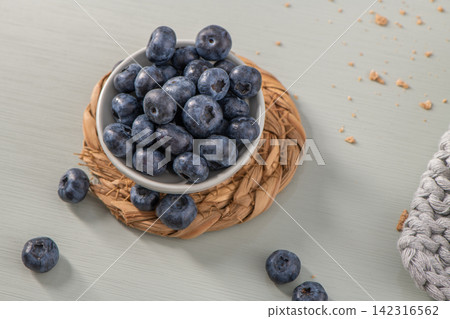 Fresh blueberries in a small white bowl on a woven placemat Fresh blueberries in a small white bowl on a woven placemat 142316562