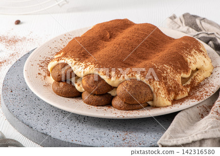 Homemade tiramisu cake on a ceramic plate with cocoa powder Homemade tiramisu cake on a ceramic plate with cocoa powder 142316580