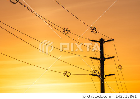 Power transmission poles and electrical distribution lines at sunset representing modern energy infrastructure and rural electrification 142316861