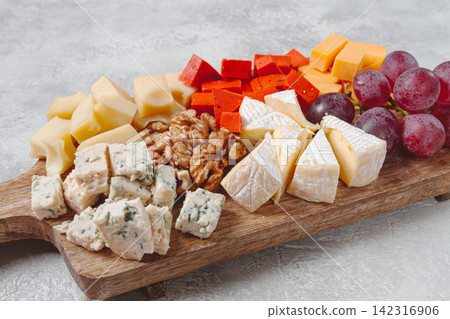 Assorted cheese on a wooden board, with grapes and walnuts, appetizer, no people. Assorted cheese on a wooden board, with grapes and walnuts, appetizer, no people. 142316906