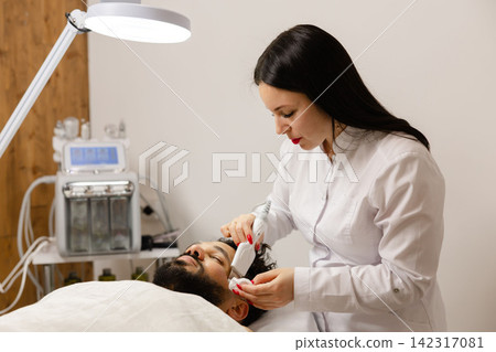 Female aesthetician performing facial treatment on man Female aesthetician performing facial treatment on man 142317081