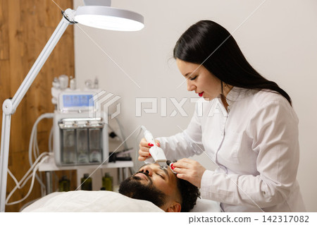 Male client receiving ultrasonic facial peeling treatment Male client receiving ultrasonic facial peeling treatment 142317082