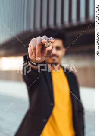 Moroccan man showing euro coin outdoors, finance concept 142317132