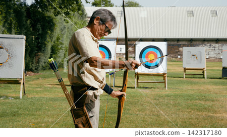 Older man practicing archery aiming for goals Older man practicing archery aiming for goals 142317180