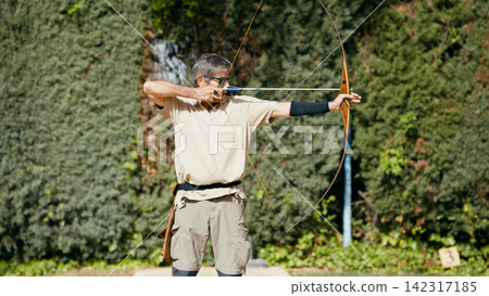 Senior man practicing archery aiming at goals Senior man practicing archery aiming at goals 142317185
