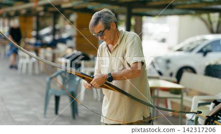 Senior man stringing longbow practicing archery hobby Senior man stringing longbow practicing archery hobby 142317206