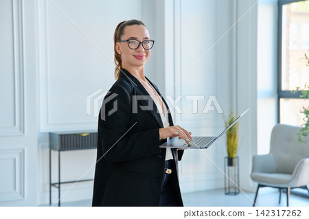 Smiling businesswoman wearing eyeglasses holding laptop standing modern office 142317262