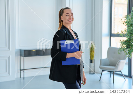 Businesswoman holding blue clipboard standing in modern office portrait Businesswoman holding blue clipboard standing in modern office portrait 142317264