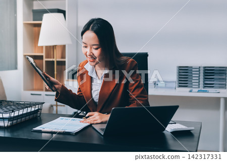 Asian businesswoman using calculator and working on laptop at modern office Asian businesswoman using calculator and working on laptop at modern office 142317331