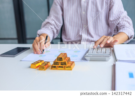 Close-up hands using calculator for gold bar trading analysis. Concept for wealth management, asset protection, and financial planning. Close-up hands using calculator for gold bar trading analysis. Concept for wealth management, asset protection, and financial planning. 142317442