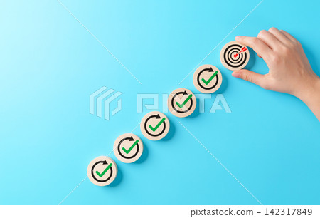 Business goal achievement concept. Hand placing target icon after completing step by step progress with check marks, represents strategic planning, performance improvement, success objective execution Business goal achievement concept. Hand placing target icon after completing step by step progress with check marks, represents strategic planning, performance improvement, success objective execution 142317849