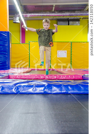 Happy active emotional preteen boy bouncing on trampoline while having fun in indoor amusement park.. High quality photo 142318050
