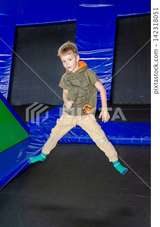 Happy active emotional preteen boy bouncing on trampoline while having fun in indoor amusement park.. High quality photo Happy active emotional preteen boy bouncing on trampoline while having fun in indoor amusement park.. High quality photo 142318051