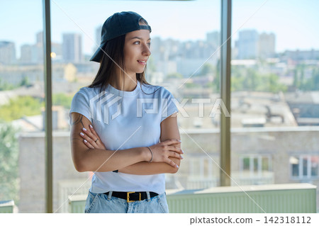 Young woman in cap looking away near panoramic window portrait Young woman in cap looking away near panoramic window portrait 142318112