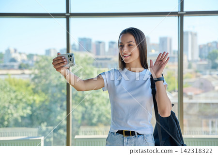 Smiling student girl having video call on smartphone by window Smiling student girl having video call on smartphone by window 142318322