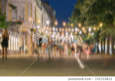 Crowd Walking on Illuminated Pedestrian Street at Night. Crowd of anonymous pedestrians walking along illuminated city street at night, intentional motion blur. Urban nightlife, movement, modern city Crowd Walking on Illuminated Pedestrian Street at Night. Crowd of anonymous pedestrians walking along illuminated city street at night, intentional motion blur. Urban nightlife, movement, modern city 142318622